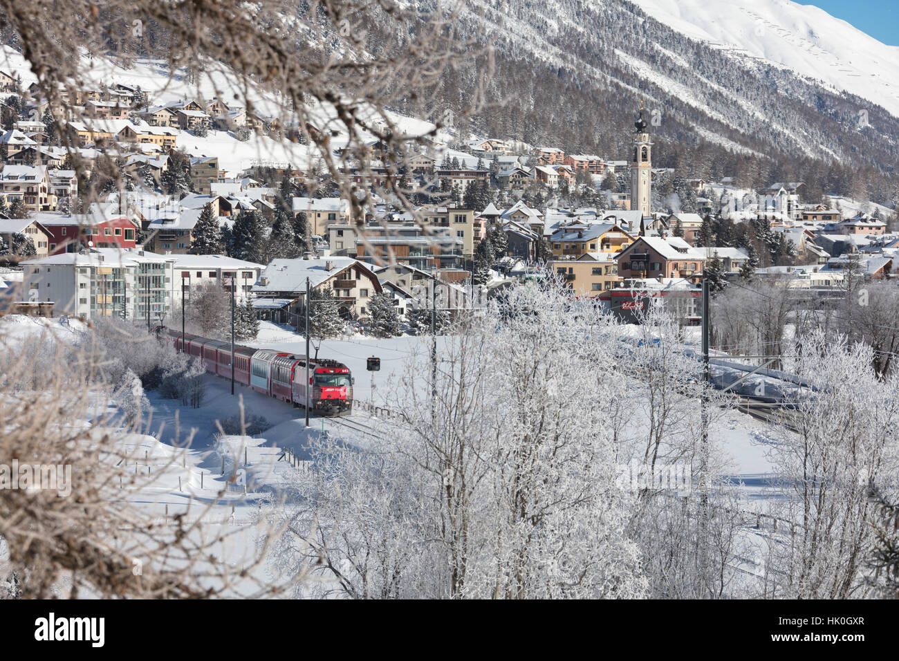 The red train runs across the snowy landscape around Samedan, Maloja, Canton of Graubunden, Engadine, Switzerland Stock Photo