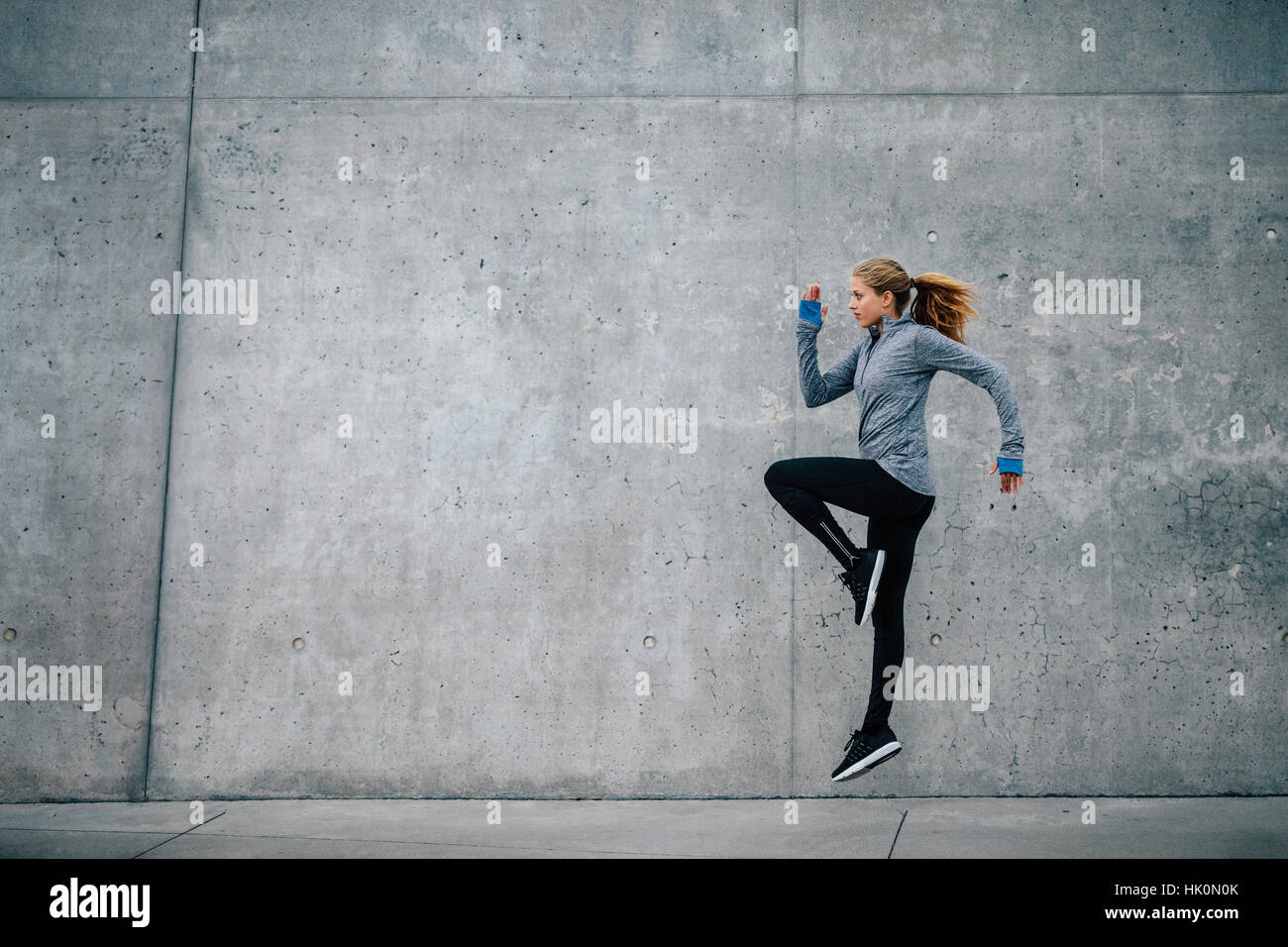 Side view shot of fitness female exercising outdoors in morning. Young woman running and jumping on city street. Stock Photo