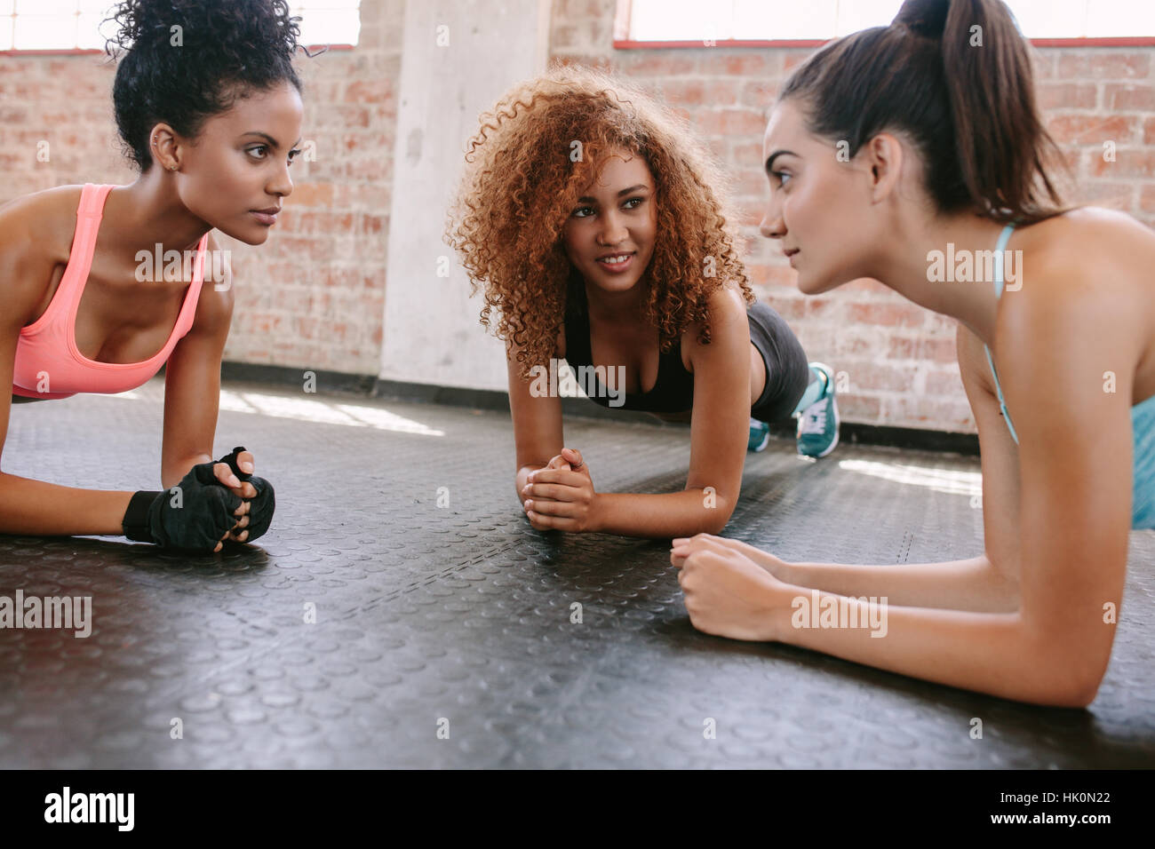 Three young women doing pushups together in gym. Group of female working out in healthclub. Stock Photo