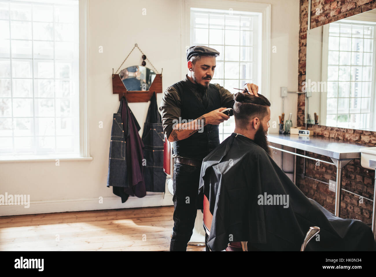 Male barber giving client haircut in shop. Hairdresser styling hair of client at salon. Stock Photo