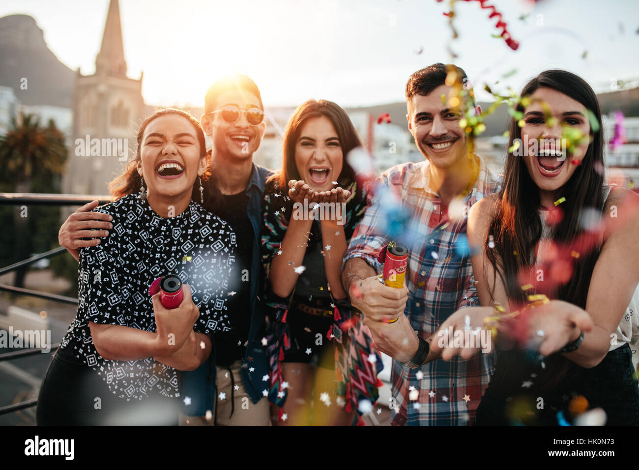 Group of friends enjoying party and throwing confetti. Friends having fun at rooftop party. Stock Photo