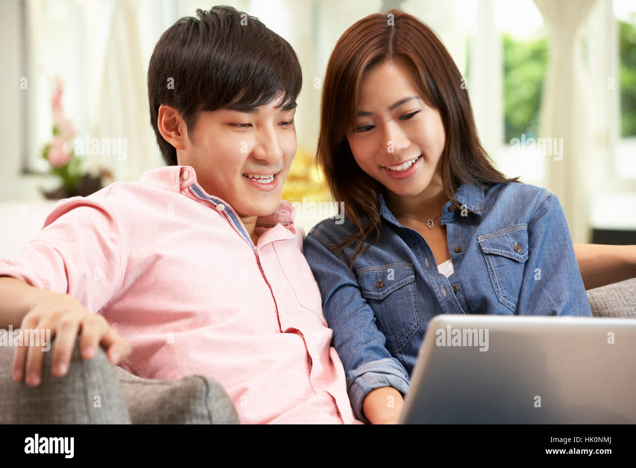 Young Chinese Couple Using Laptop Whilst Relaxing On Sofa At Home Stock ...