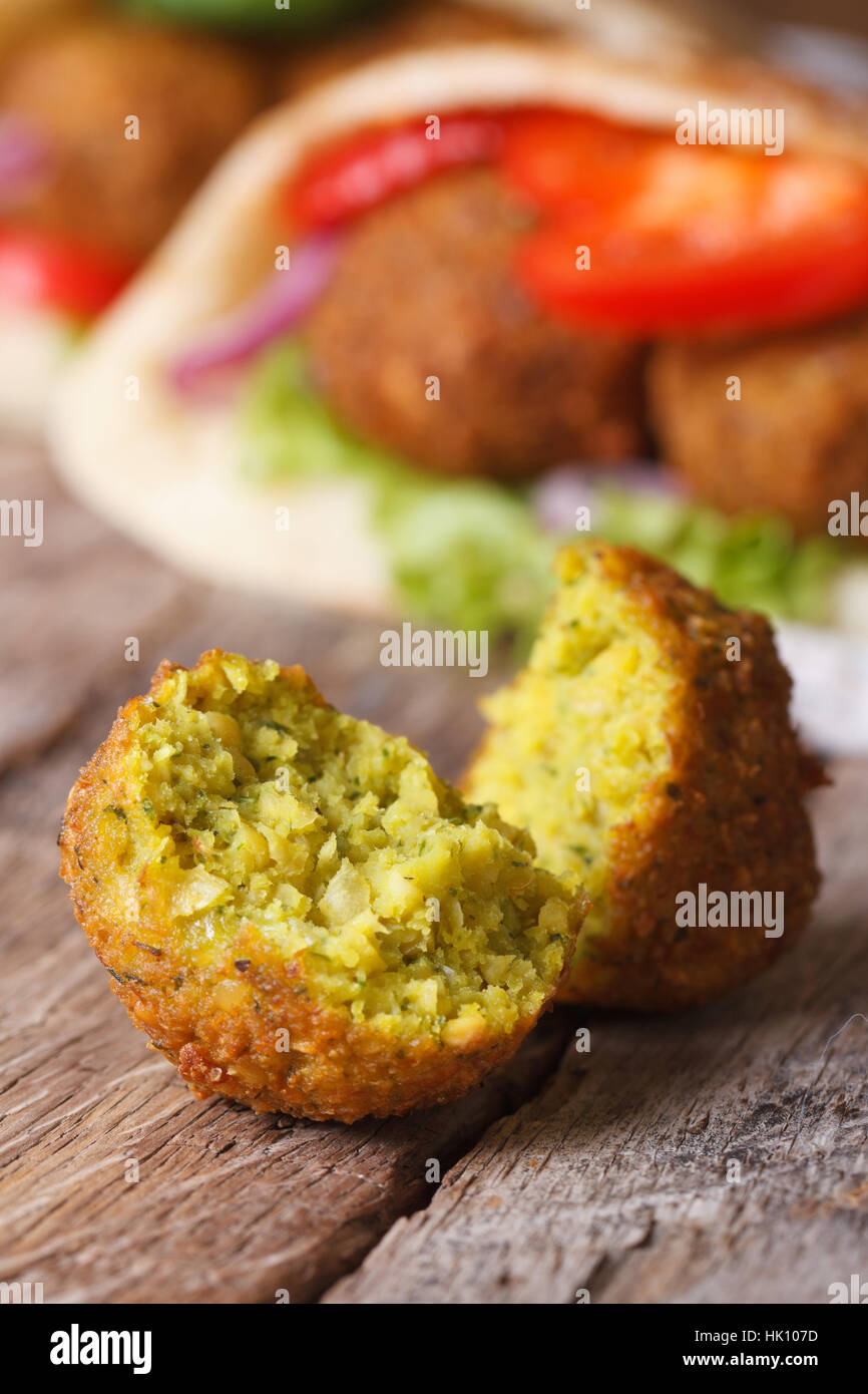 falafel macro on an old wooden table against the background of pita bread with vegetables vertical Stock Photo