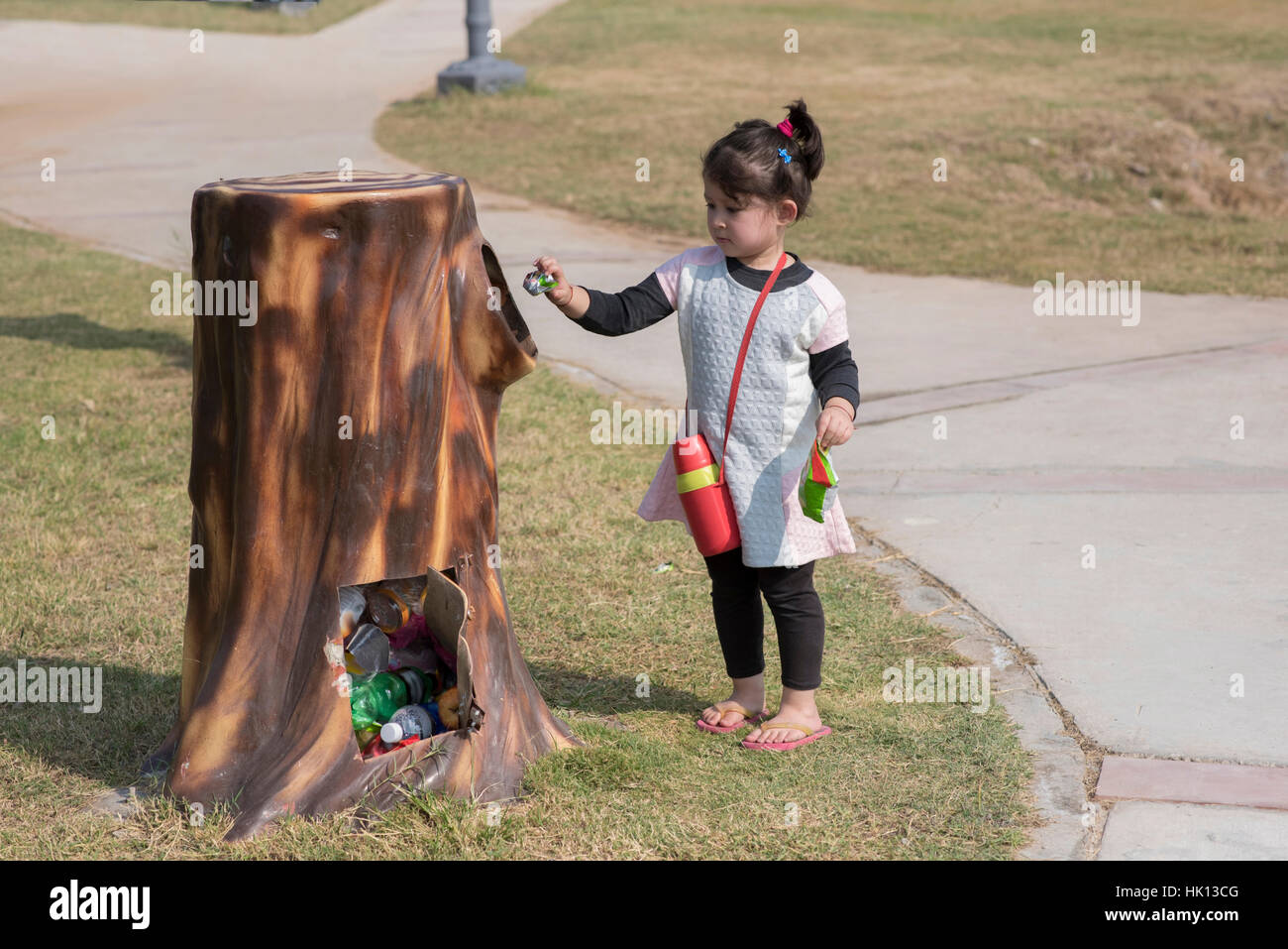 Cute little girl putting waste in the bin outdoor in a park. Stock Photo