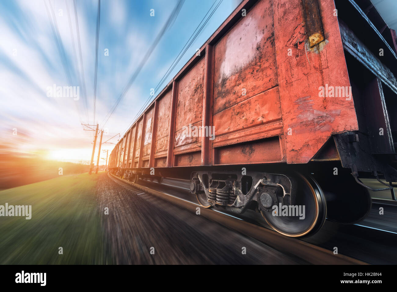 Railway station with cargo wagons and train in motion against sunny sky. Concept industrial landscape at sunset. Railroad. Stock Photo