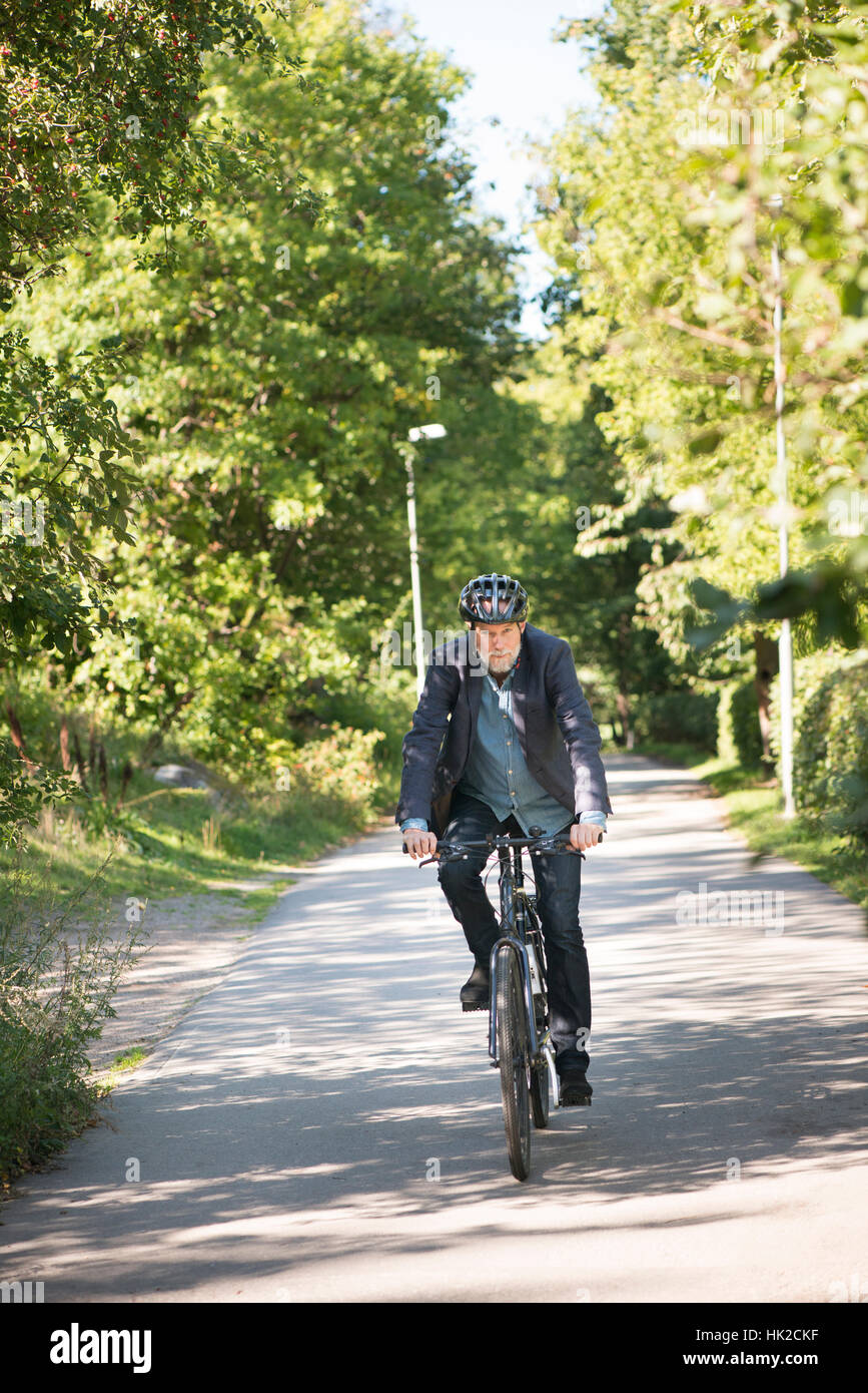 Old man with bicycle helmet riding a bike. Summer lifestyle moment with active elderly person living a healthy life. Stock Photo