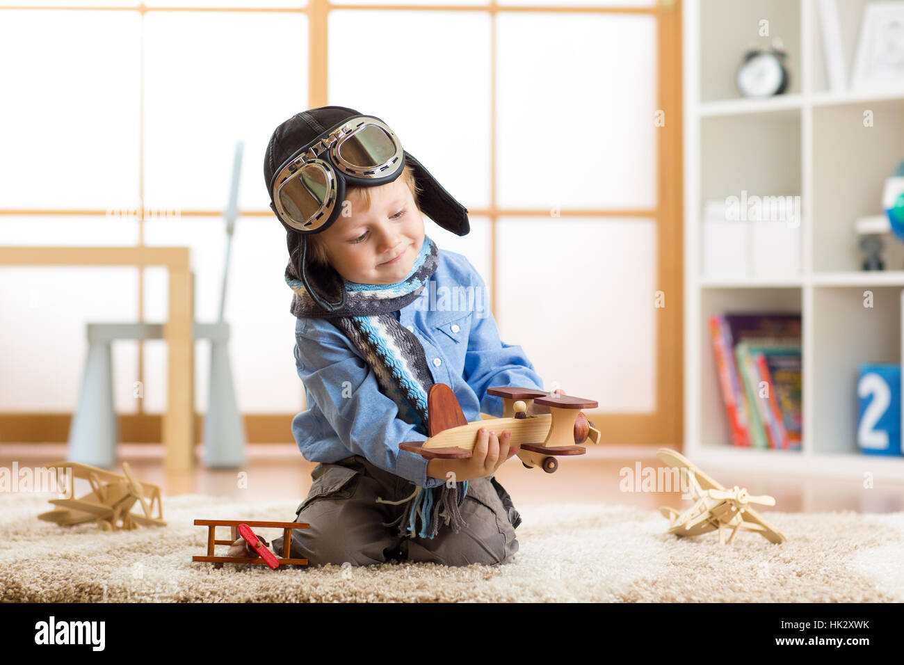 Little kid boy dreams be an aviator and plays with toy airplanes sitting on floor in nursery room Stock Photo