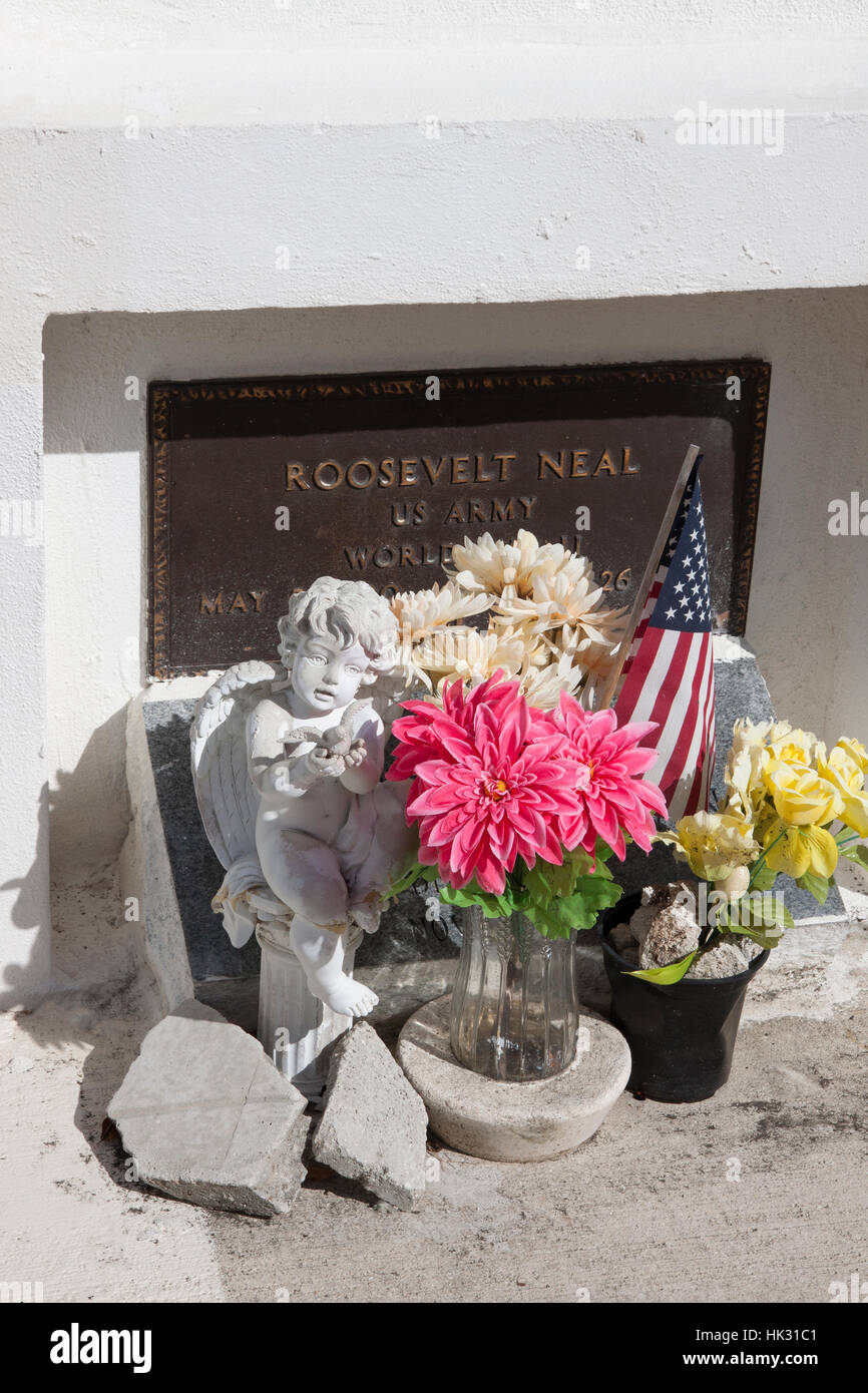 Cemetery grave site with flowers, statue, and flag in remembrance. Stock Photo