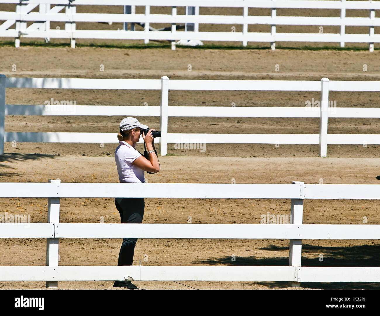 Woman photographer with camera and telephoto lens surrounded by white wooden fences. Stock Photo