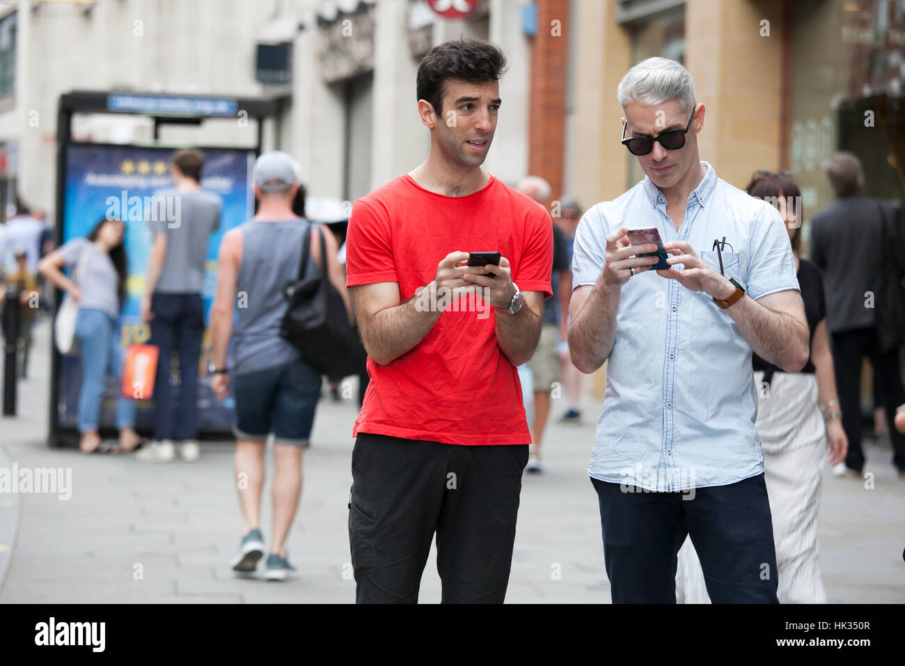 LONDON, UK - August 27, 2016: Composite image of two friends standing to the side slightly sending texts Stock Photo