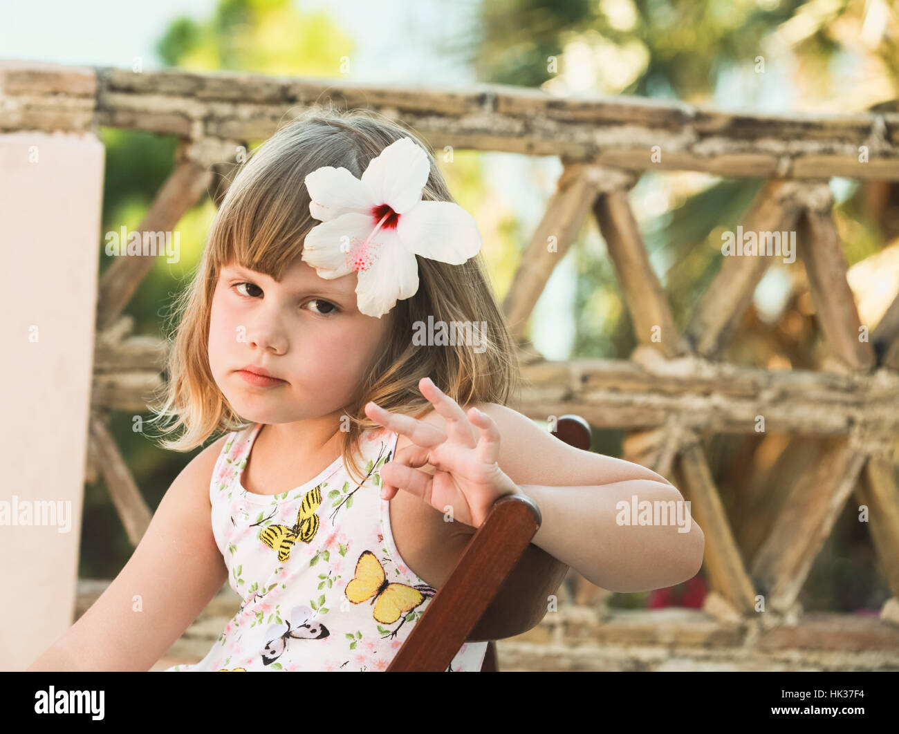 Serious Caucasian little girl with white flower in hair, outdoor portrait Stock Photo