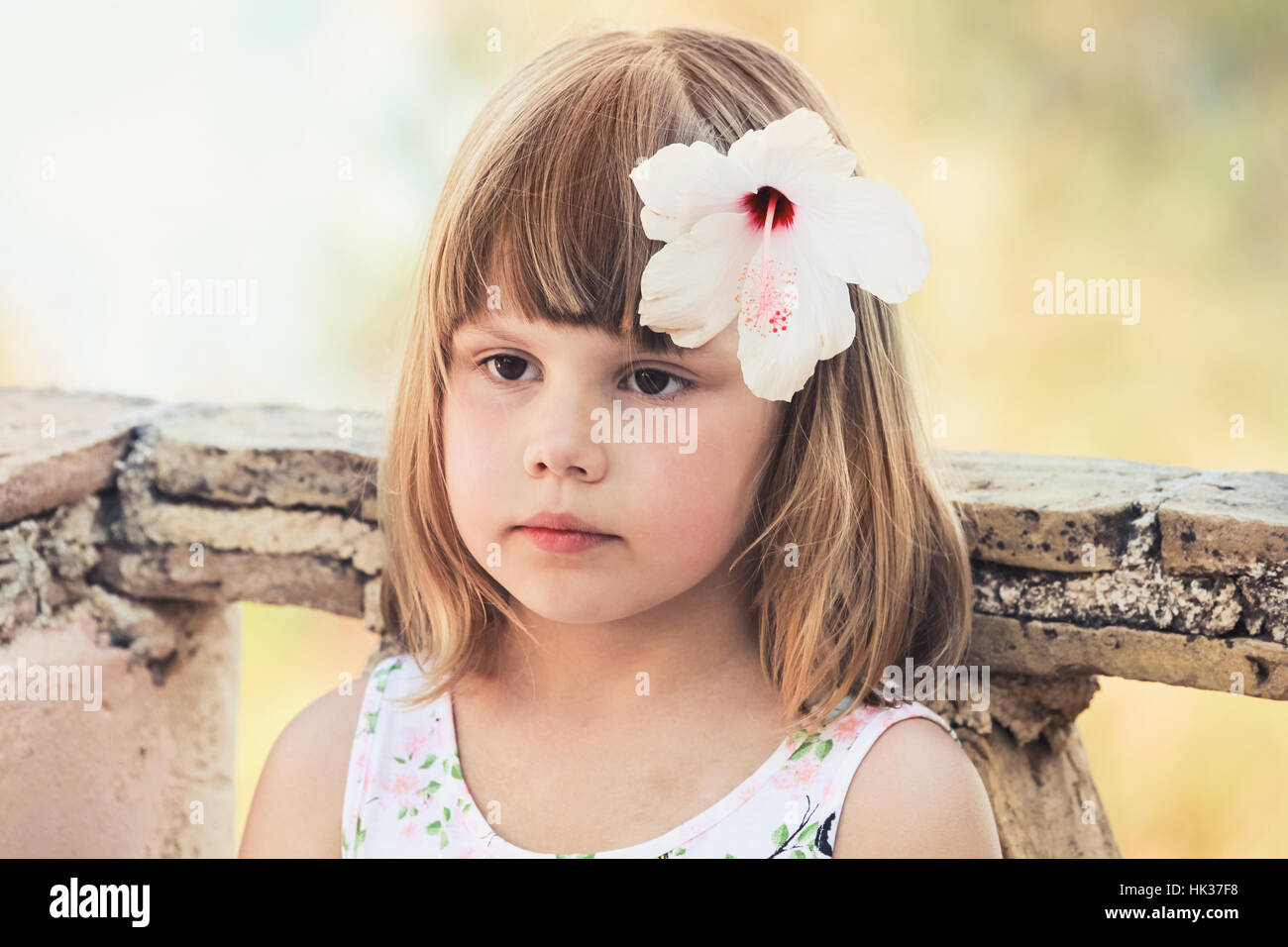Serious Caucasian little girl with white flower in hair, close-up outdoor portrait, photo with old style tonal correction filter effect Stock Photo