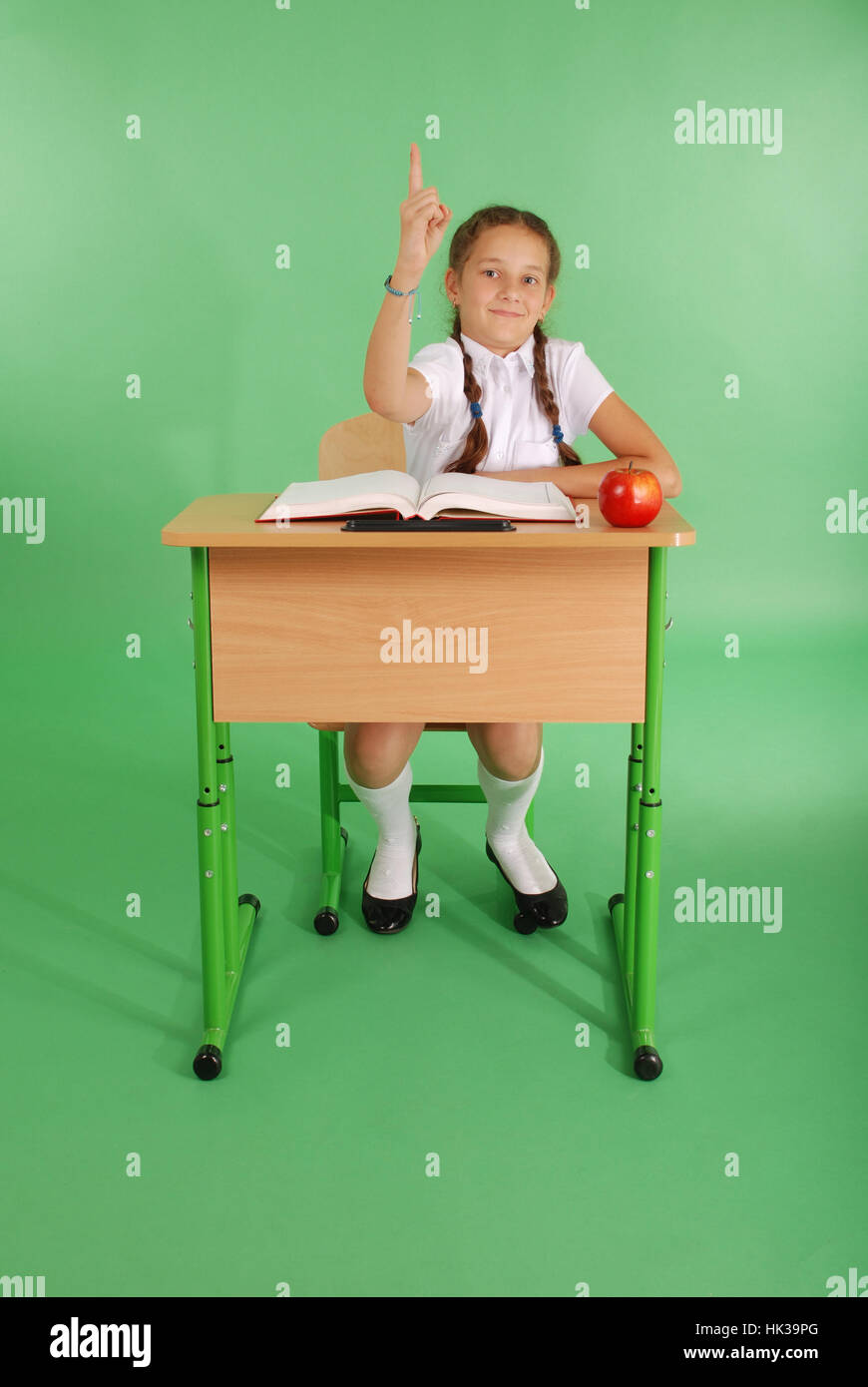 Girl in a school uniform raising hand to ask question isolated on green