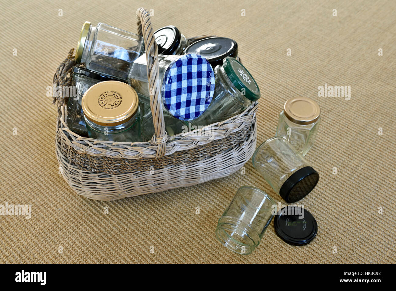 Empty glass jars in vintage wicker basket with some fallen on floor, for reuse in jam making or recycling Stock Photo