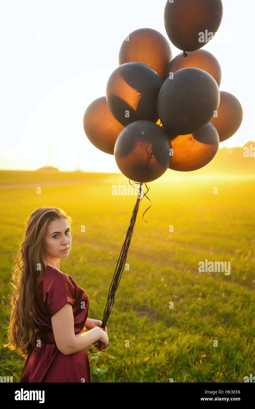 chic woman in a red dress with black balloons over beautiful sunset background Stock Photo
