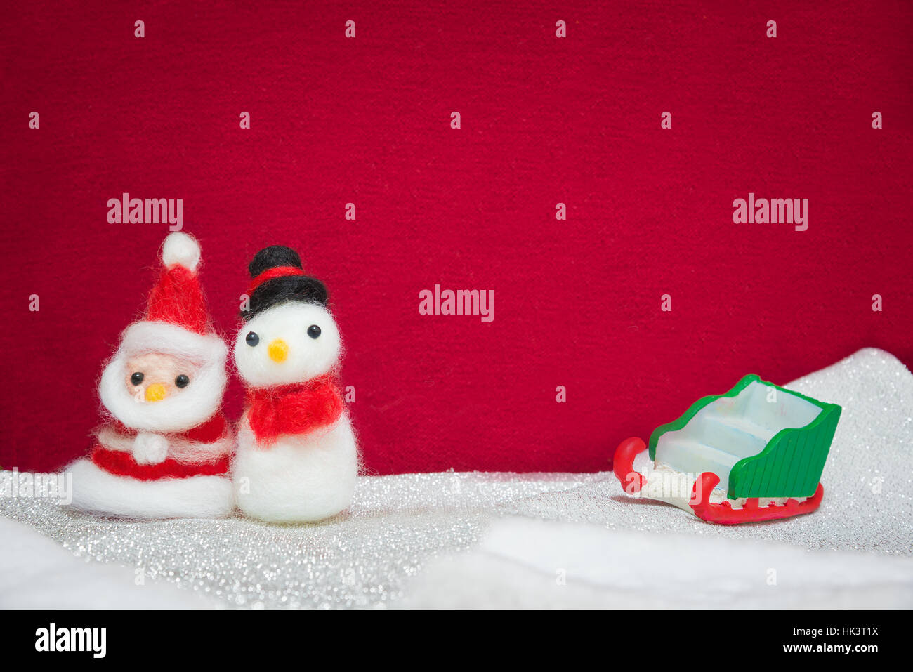Santa claus, snowman wool doll and greed sled on snow set up with red cloth backdrop, happy new year and christmas concept background Stock Photo