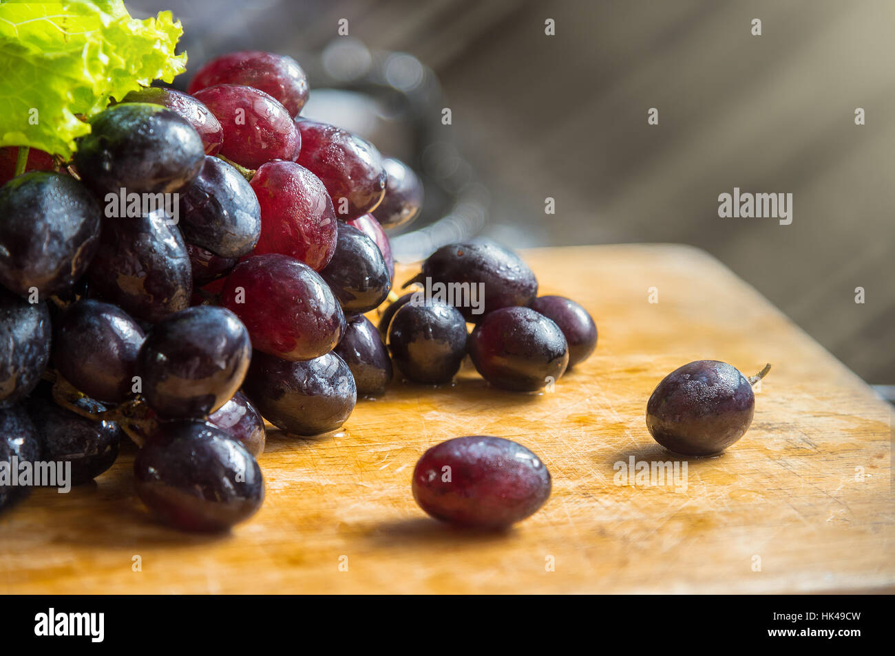 Bunch of red, black, purple grapes lay on wooden tables with light ray background, selective focus Stock Photo