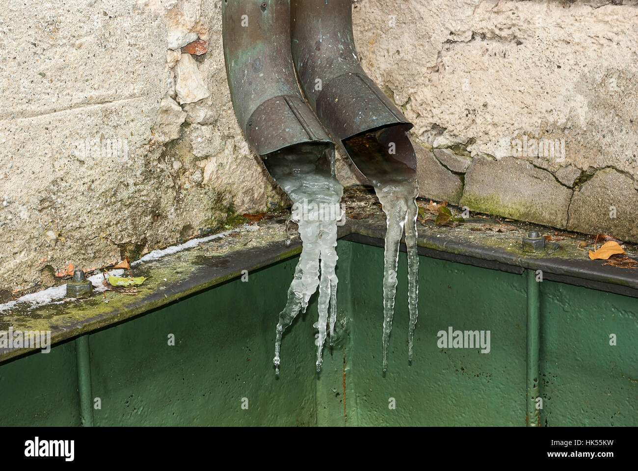 Frozen water shapes icicles at the end of rain pipes. Stock Photo
