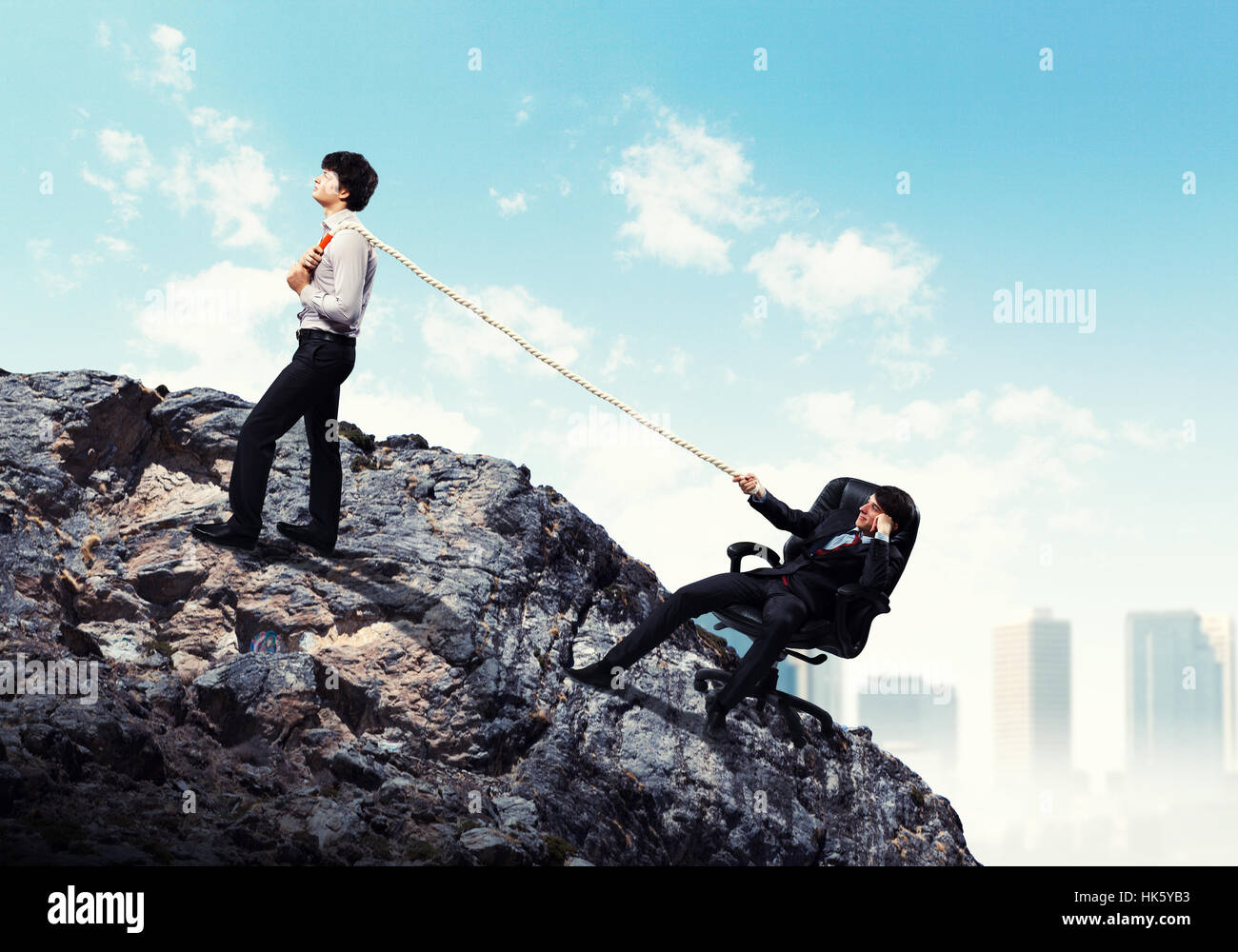 Pulling Against Rope Image of two young businessmen pulling rope atop of mountain against ...