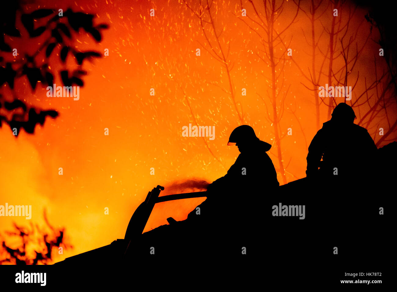 Silhouettes of firemen on the roof of a burning house Stock Photo