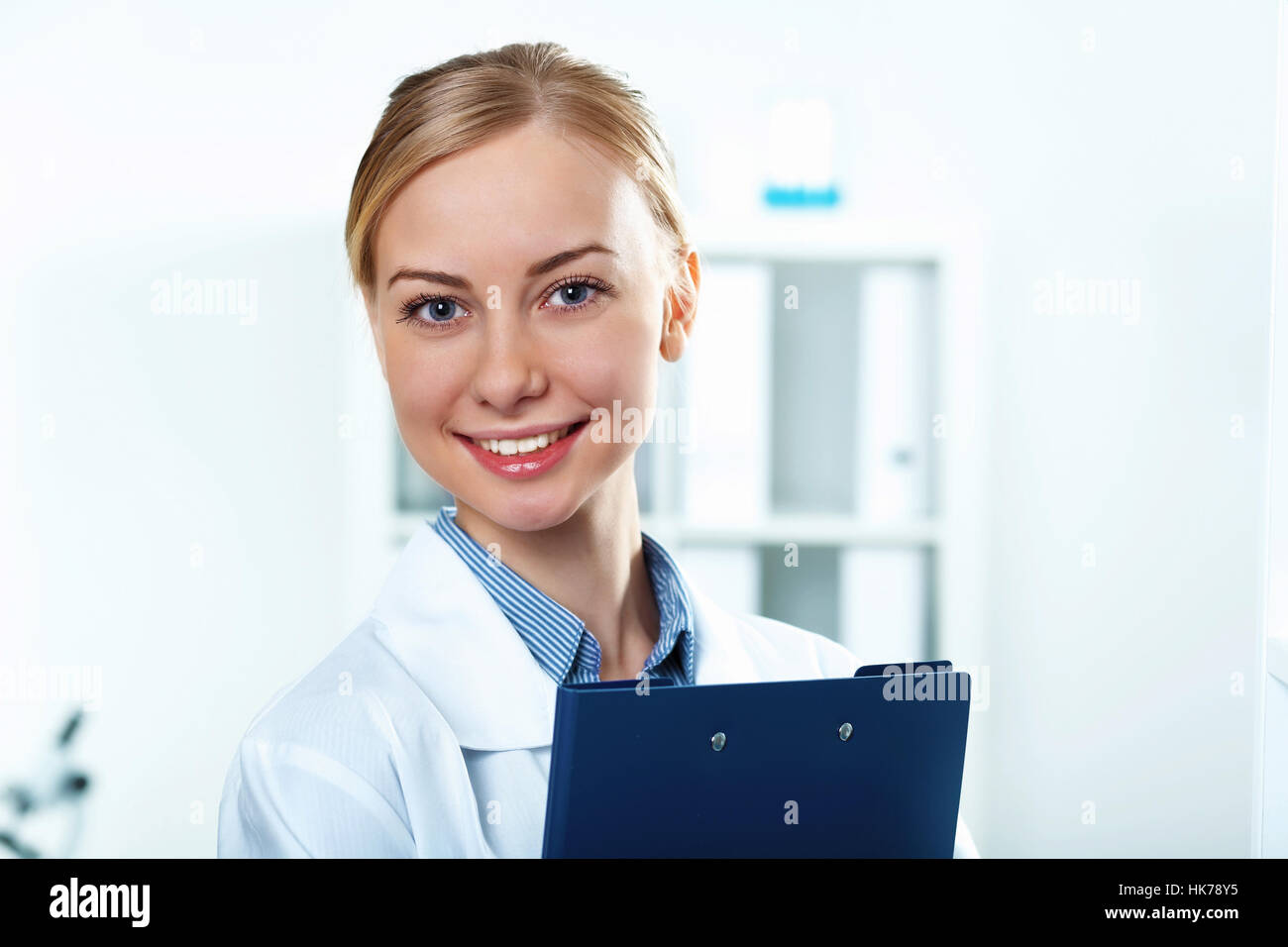 Young doctor in white uniform standing and holding papers Stock Photo ...