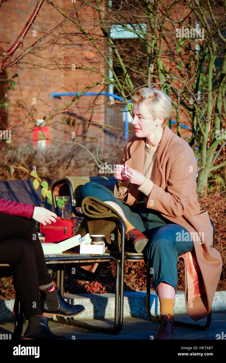 A well dressed blonde woman chats to a girlfriend on a park bench Stock Photo