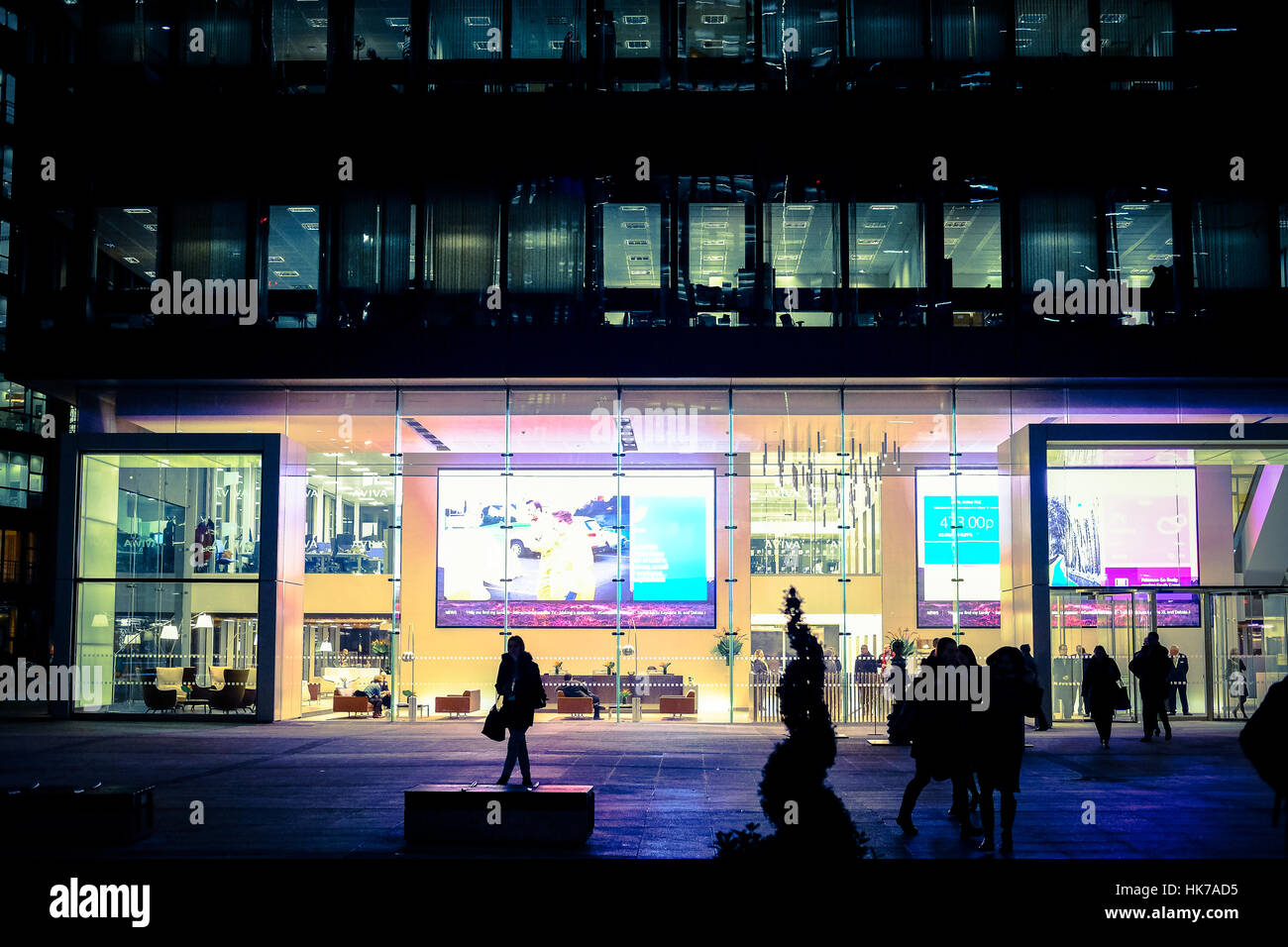 Silhouetted people walk in front of a corporate office building at night Stock Photo