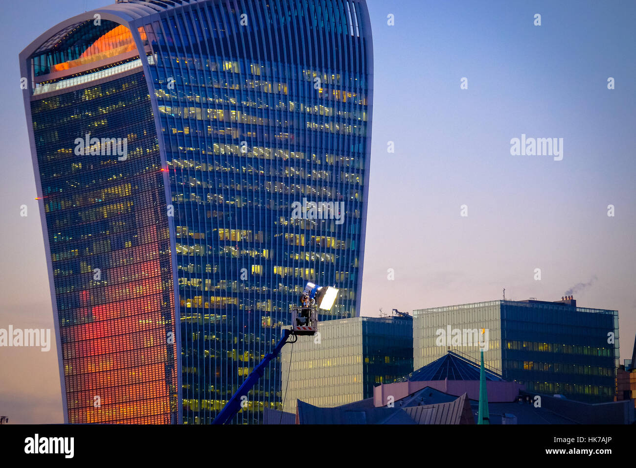 A sunset is reflected off of the windows of a futuristic looking office building whilst a lighting rig shines on a movie set. Stock Photo