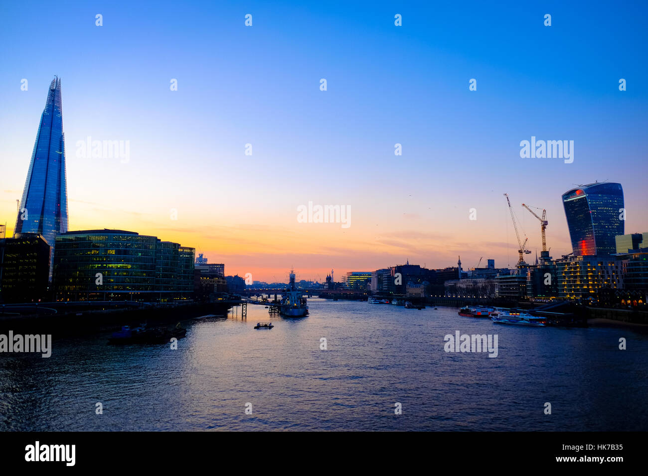 The sun sets over London's River Thames against a skyline of futuristic looking office buildings. Stock Photo