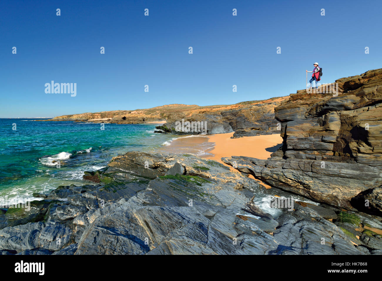 Woman standing at the edge of a rocky cliff looking to natural beach Stock Photo