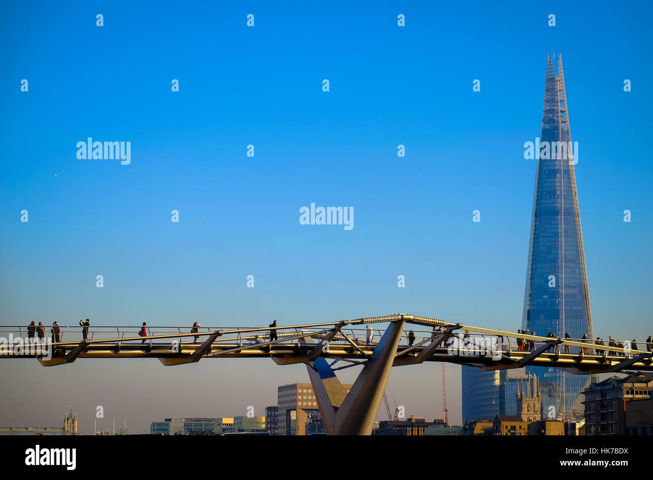 A crowd of people walk over London's Millennium Bridge, with The Shard office building in the background. Stock Photo