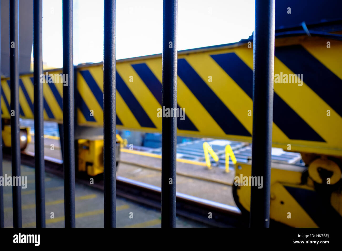 Black railings guard a crane system with a hazard pattern painted on it. Stock Photo