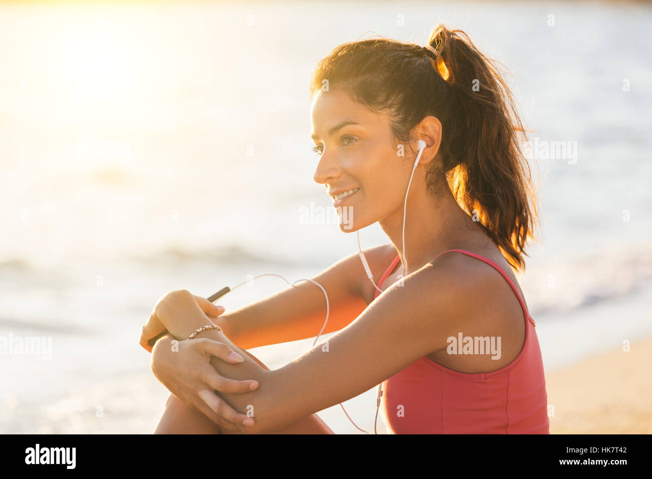 Beautiful young girl is listening music with earphones on the beach at sunset Stock Photo