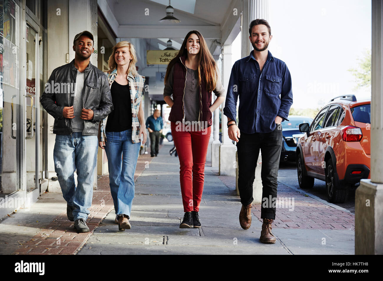Two young men and two young women walking along a sidewalk, smiling into shot. Stock Photo