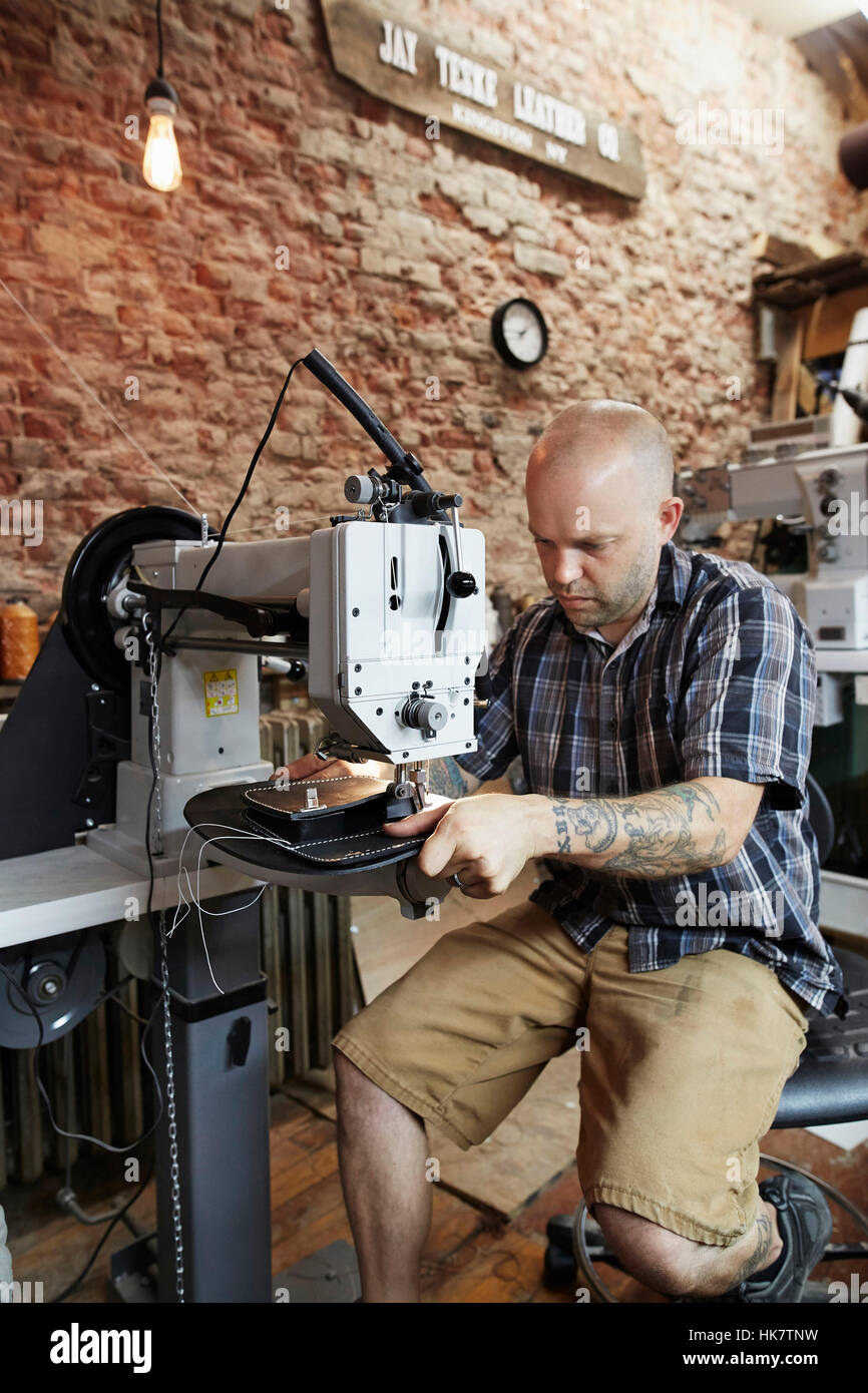 A leather worker, craftsman using an industrial sewing machine on leather material, making a bag