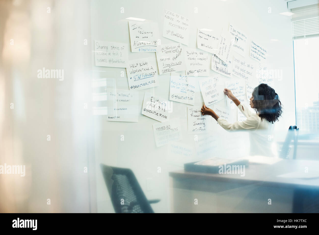 A woman standing in an office arranging pieces of paper pinned on a whiteboard. Stock Photo