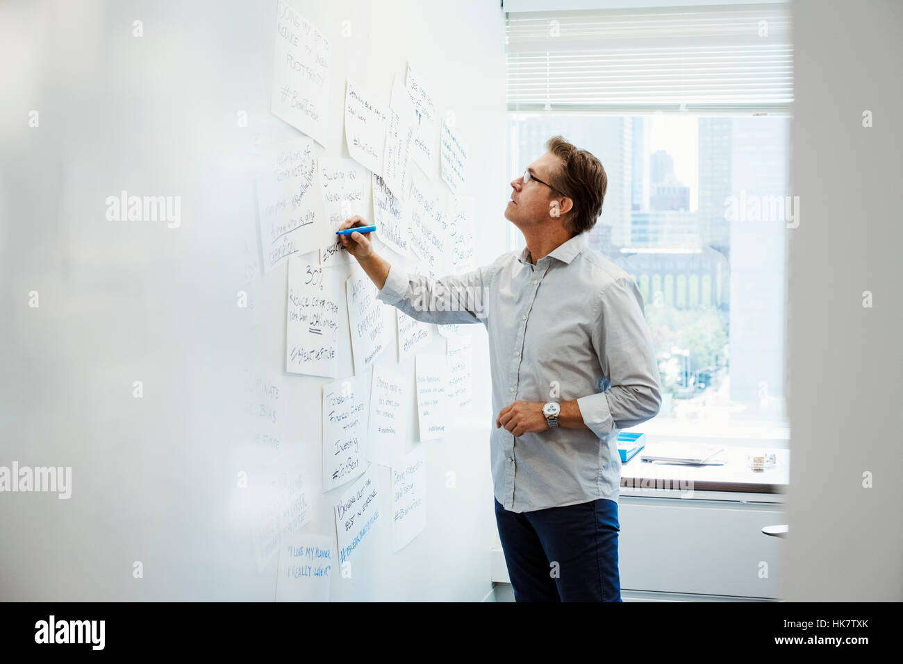 A man standing in an office writing on pieces of paper pinned on a whiteboard. Stock Photo