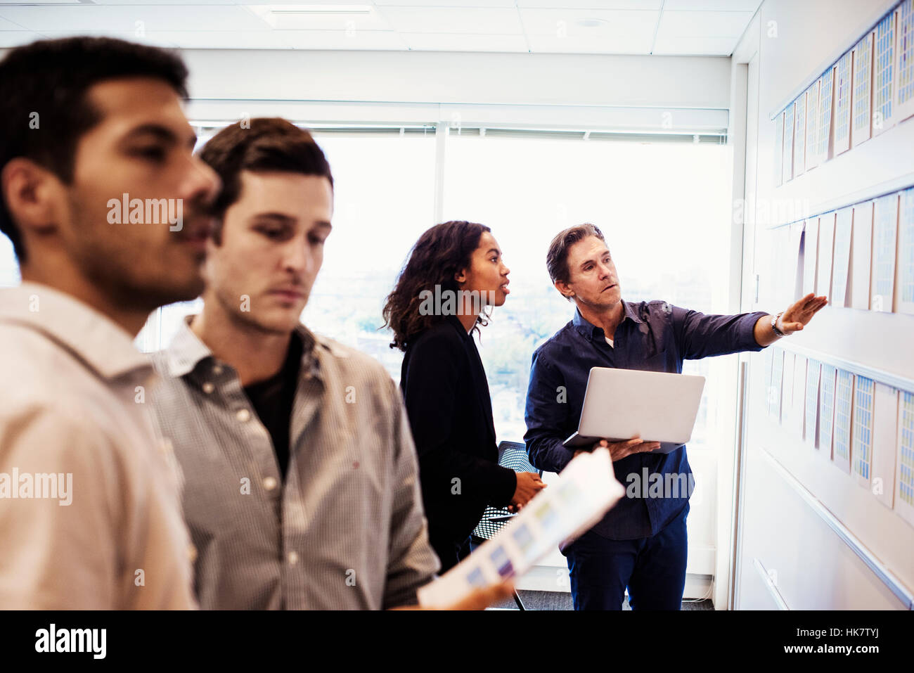 A woman and three men standing in an office looking at a display on a wall. Stock Photo