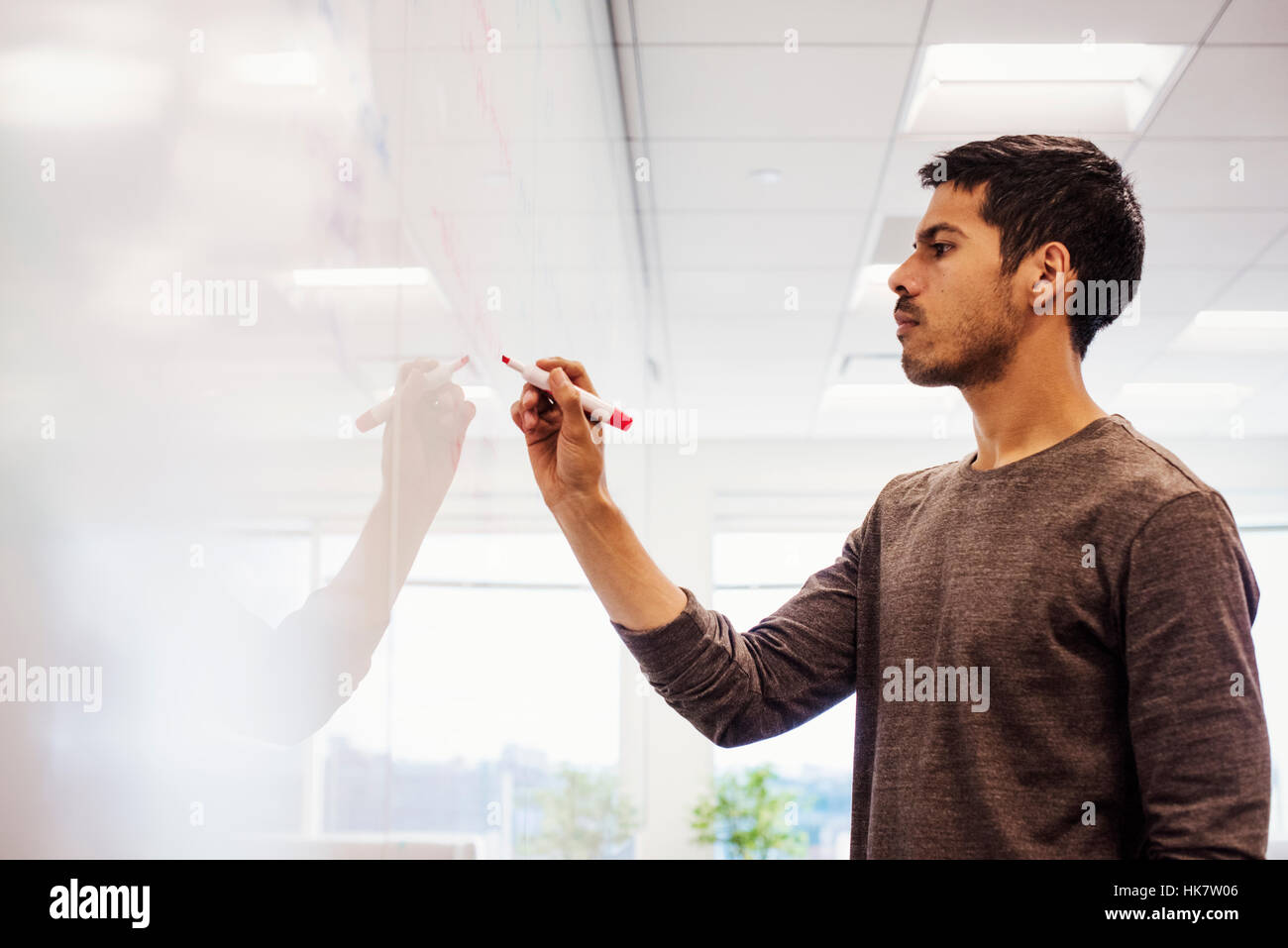 A man standing in a classroom writing on a whiteboard. Stock Photo