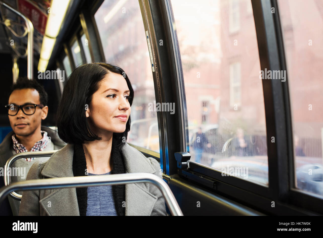 A young woman sitting on a train looking out of the window at an urban landscape, with a man sitting behind her looking away. Stock Photo