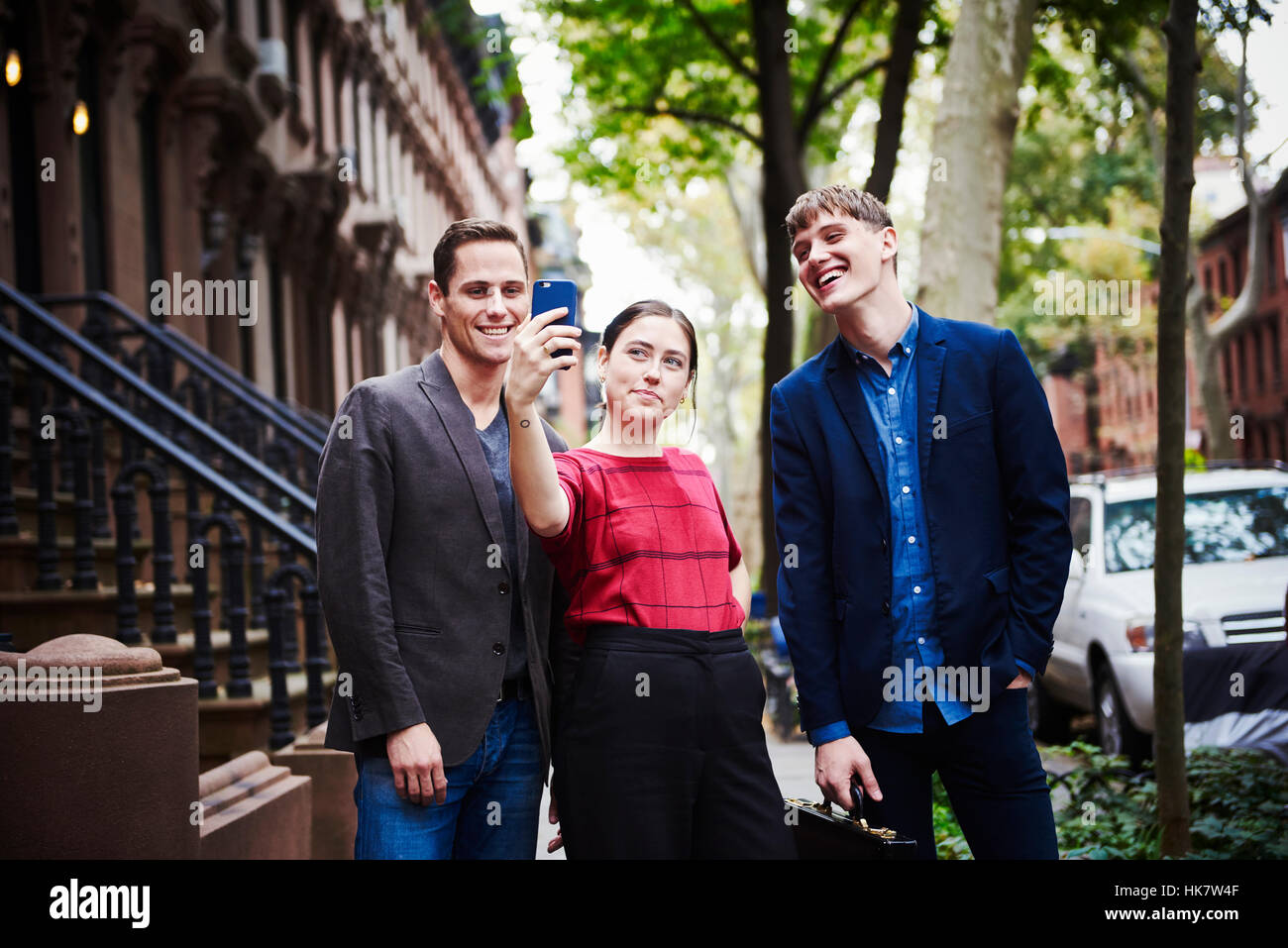 Two young men and a young woman posing for a selfie taken with a cellphone in a city street. Stock Photo