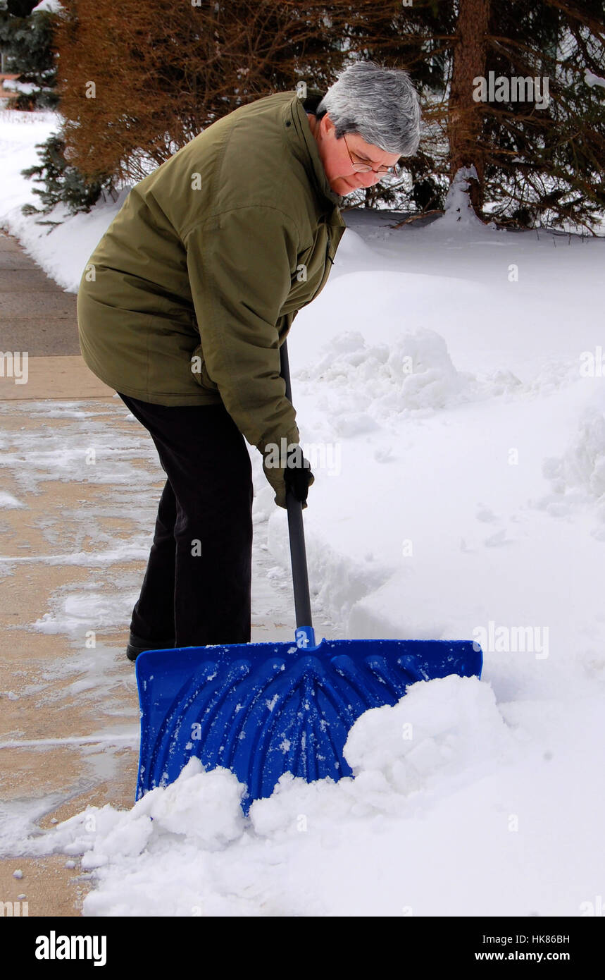 middle aged woman shoveling snow off sidewalk Stock Photo