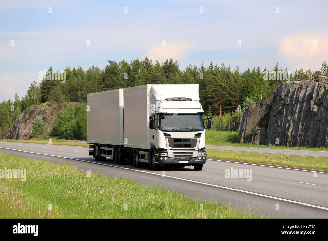 Big white cargo truck transports goods along motorway on a beautiful