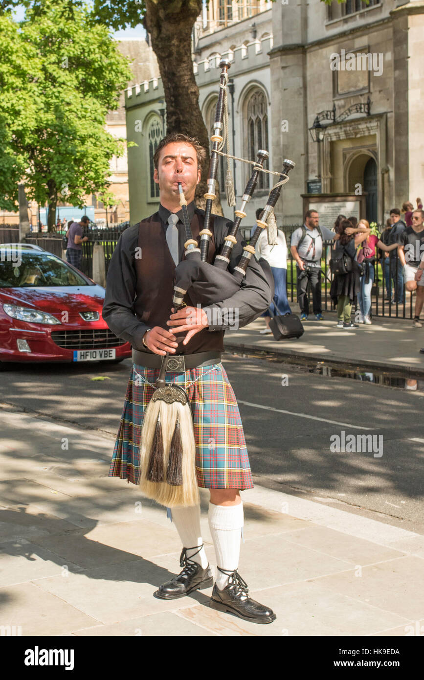 A busker wearing a kilt playing bagpipes for tourists close to