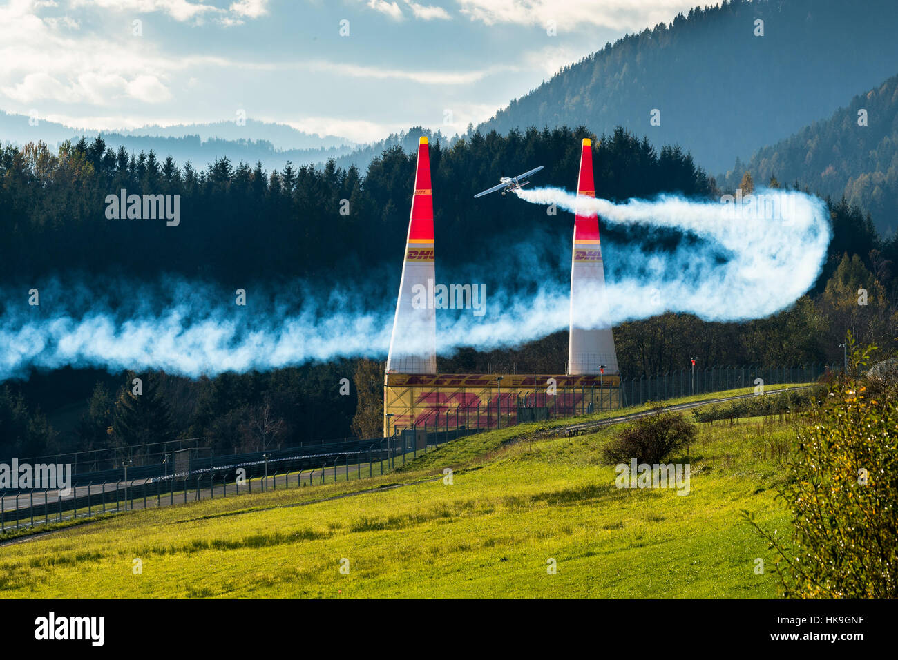 A stunt flying aeroplane, releasing smoke, is flying through 2 pylons ...
