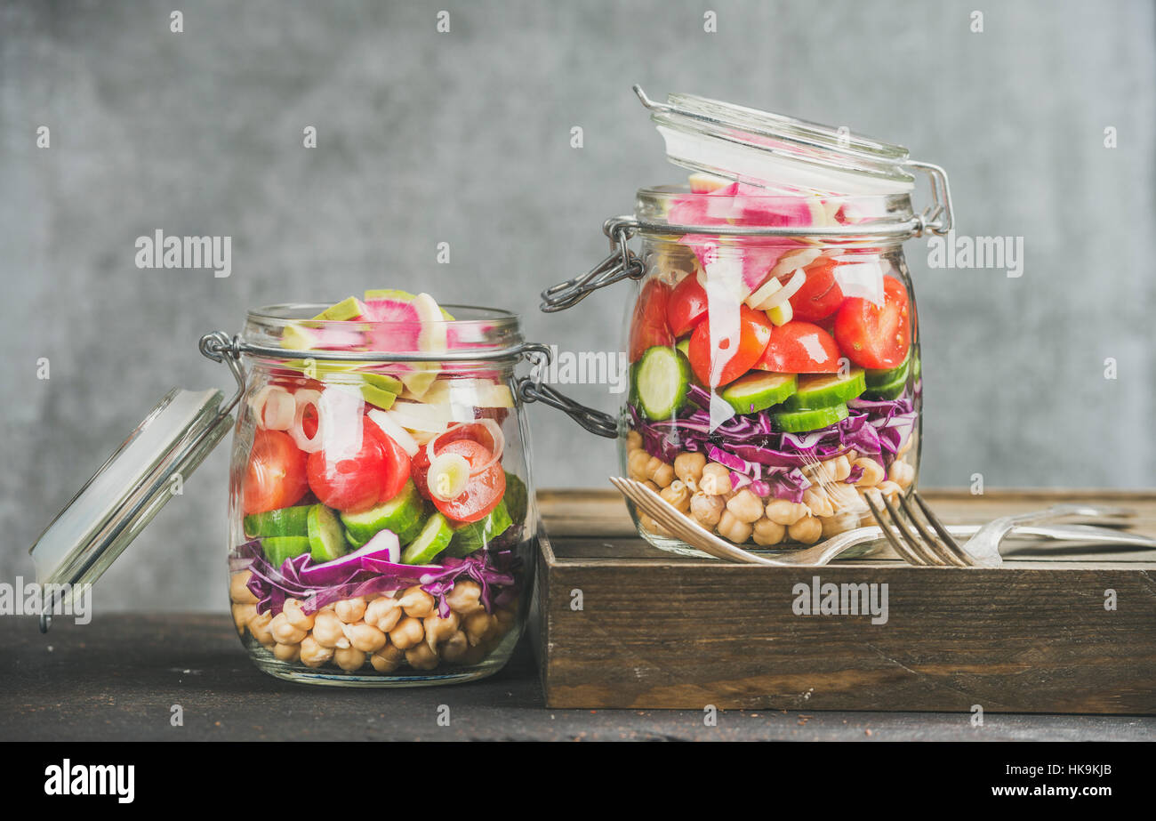 Healthy take-away lunch jars. Vegetable and chickpea sprout vegan salad in glass jars, grey concrete wall background, copy space, selective focus. Cle Stock Photo