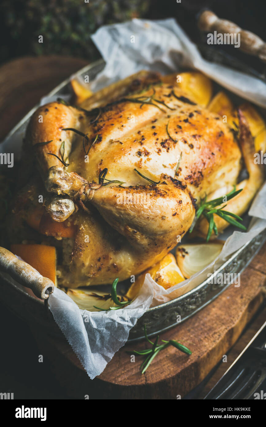 Close-up of Christmas roasted whole chicken stuffed with oranges, bulgur and rosemary in vintage metal tray over rustic wooden board background. Selec Stock Photo