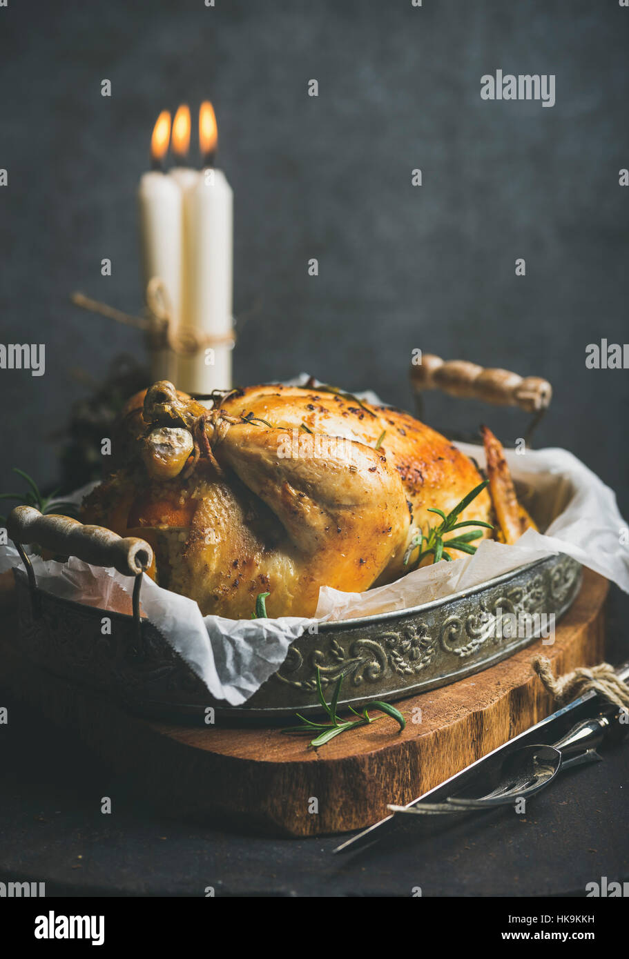 Christmas table set with oven roasted whole chicken with oranges, bulgur and rosemary, decorative candles on wooden board, grey concrete wall backgrou Stock Photo