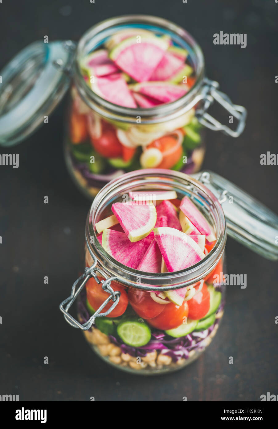 Healthy take-away lunch jars. Vegetable and chickpea sprout layered vegan salad in glass jars over dark scorched wooden background, selective focus. C Stock Photo