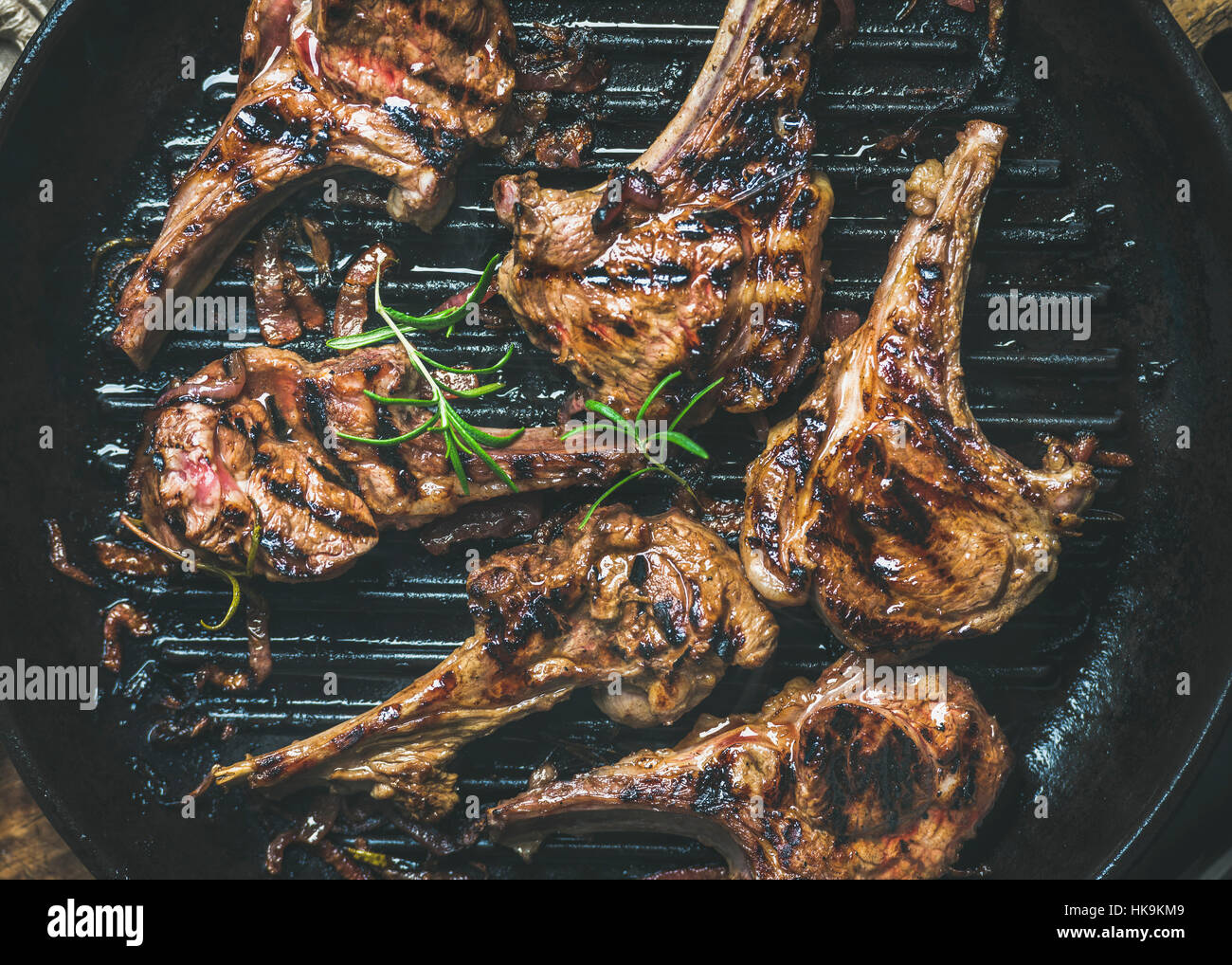 Barbecue dinner. Grilled lamb meat chops with onion and rosemary in black cast iron pan, top view, close-up. Slow food concept Stock Photo